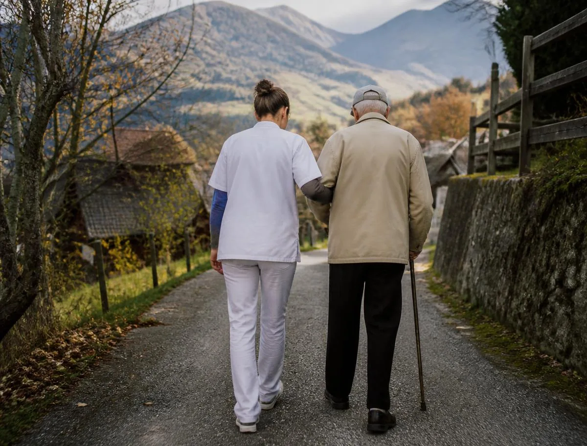 Begleitung und tägliche Spaziergänge Betreuerin begleitet einen älteren Mann bei einem Spaziergang in einem Schweizer Dorf